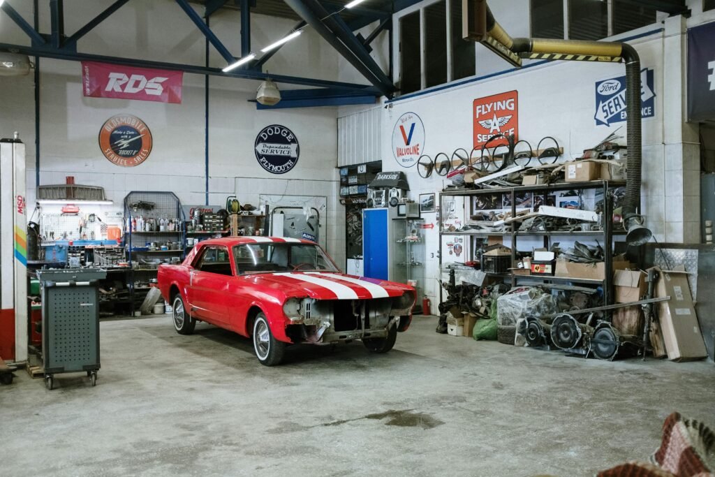 A vintage red car undergoing restoration in a well-equipped workshop with various tools and auto parts.