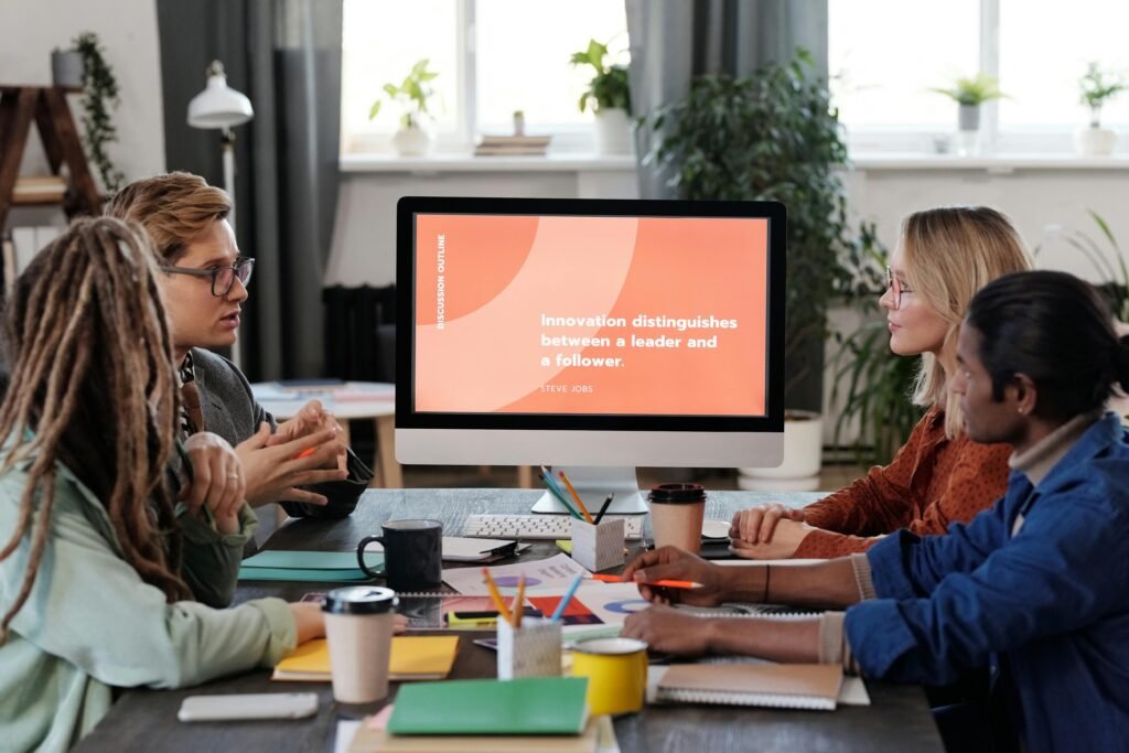 A multicultural team collaborating in an office, discussing a project with a visible monitor.